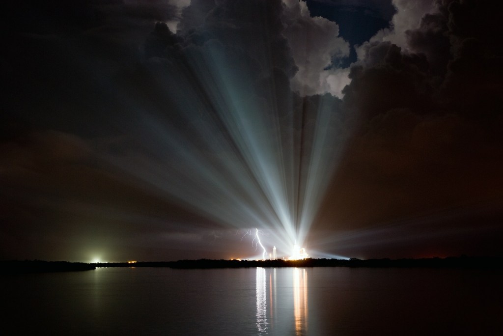 Space shuttle taking off with lightning and cloud reflections over the bay