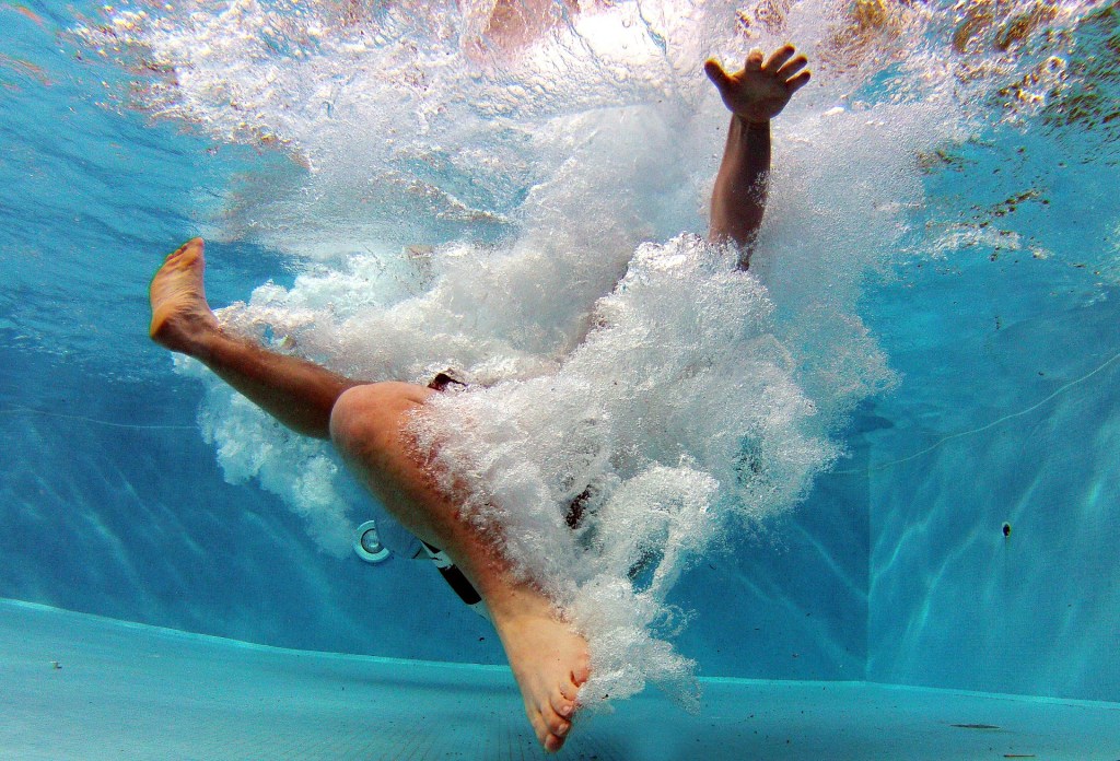 Person underwater in a pool surrounded by bubbles from jumping in