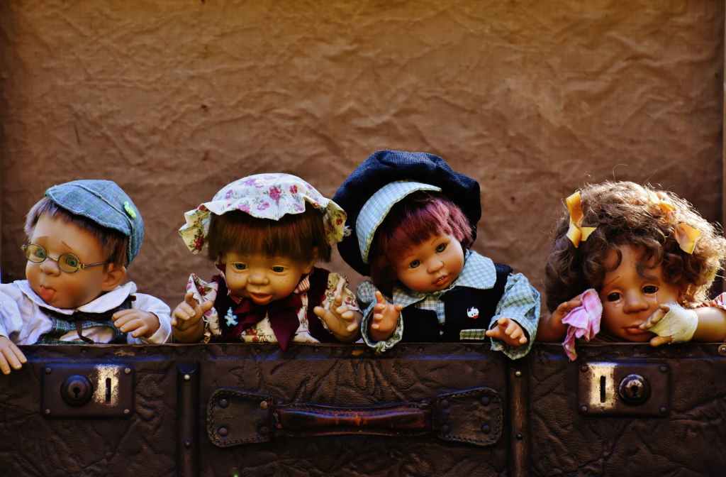 Four toy realistic dolls looking over a suitcase