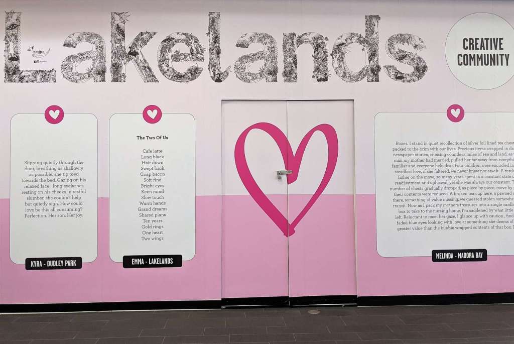 Image of a wall with pink graduated background, the word 'Lakelands' illustrated in black-and-white, and three creative writing pieces as large posters on the wall. Heart in the centre.