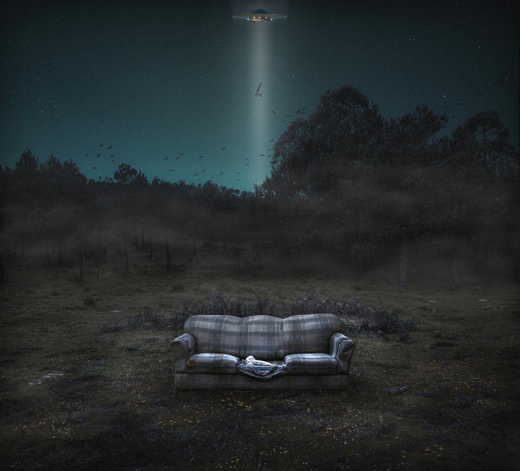 Foggy, dark landscape of a forest, with an old, ripped, striped couch in the foreground (open air), and a UFO in the night sky 'beaming up' what looks like a pram/buggy.
