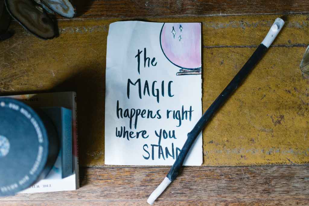 A stick painted black with white on each end lying on a note that says The Magic Happends Right Where You Stand with a drawing of a crystal ball