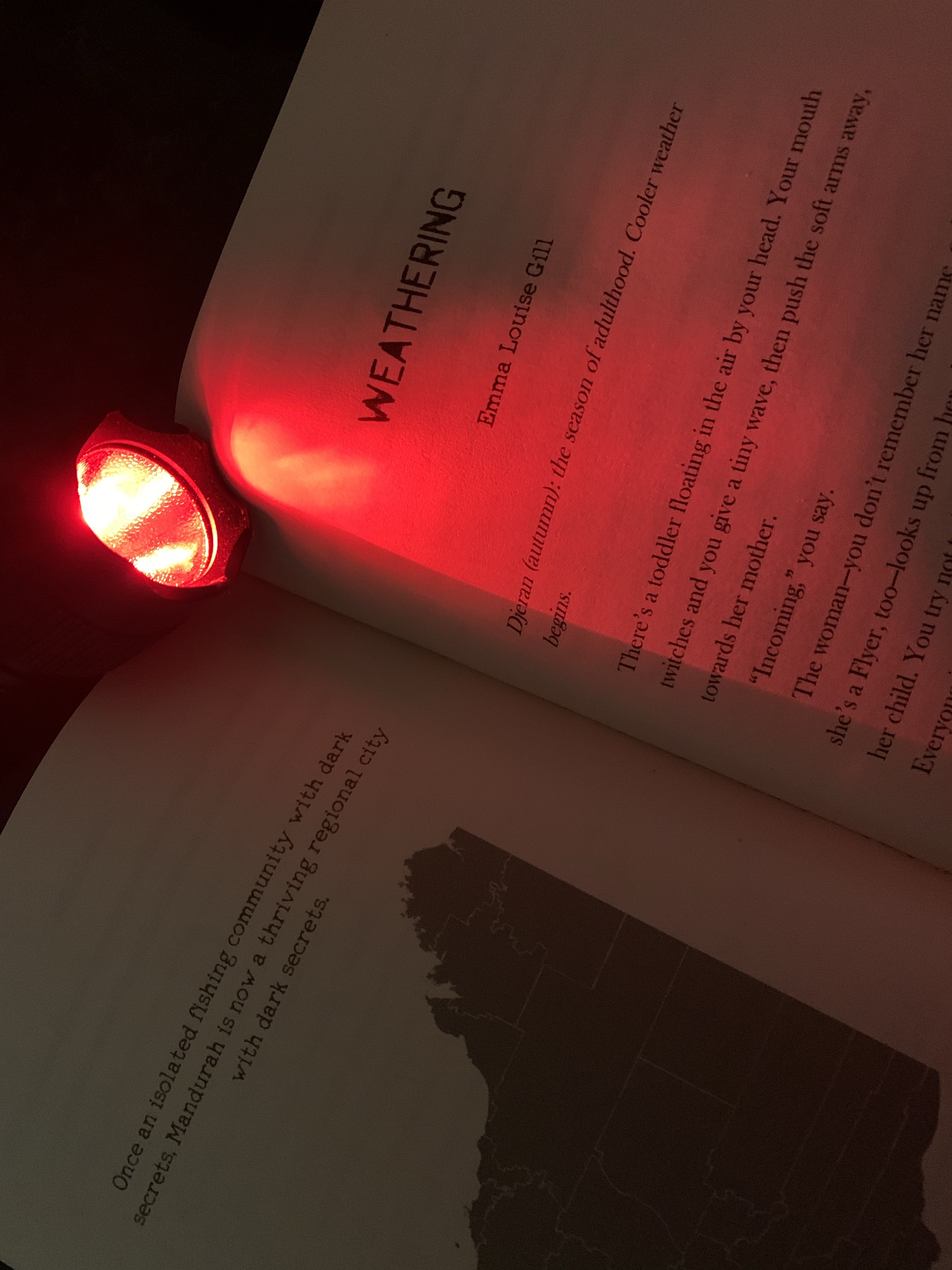 Book open to Weathering by Emma Louise Gill, red light torch shining on it. 