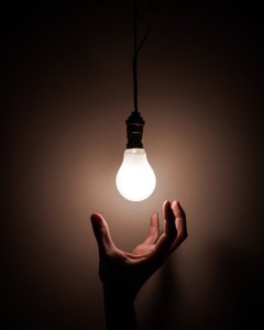 Hand open beneath a naked lightbulb that is glowing